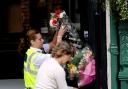 Police help a woman arrange floral tributes attached to the gates  outside the flats in Norton, where jockeys Jamie Kyne and Jan Wilson lost their lives