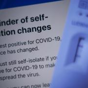 A positive lateral flow test cassette placed next to advice from the NHS COVID app (PA)