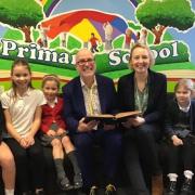 Jenny Rogers and Jonathan Green sitting with some of the youngest and oldest members of the school. They are holding the school log book which was started 155 years ago when the original school opened in what is now Copmanthorpe Old School Medical