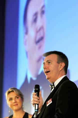 David Rennie of Nestlé speaking on stage after receiving The Press Business of the Year 2011 Award, watched by ITV presenter Kate Walby.
