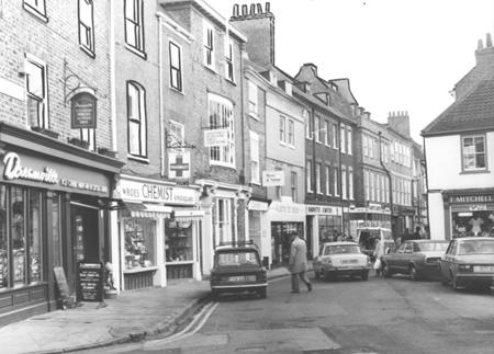 Colliergate in 1981.  Dreamville Ice Cream Parlour , Wroe's Chemists, Berry & Nutton opticians, and Austins for value are shops (from left to right) before Barnitts.  The sport shop on the other side of the street is T. Mitchell's.