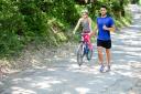 young woman riding bicycle beside a young man running in countryside in summer.