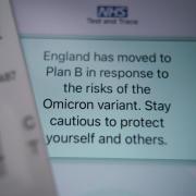 A positive lateral flow test cassette placed next to advice from the NHS COVID app on an iPhone, in London. Photo via PA.