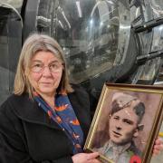 Celia standing by the rear gun turret of the Halifax Mk III bomber at the Yorkshire Air Museum, holding a photo of her uncle Edwin Bowen