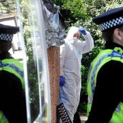 A forensics officer works in the back garden of the house in Burnholme Grove as a PCSO guards the scene